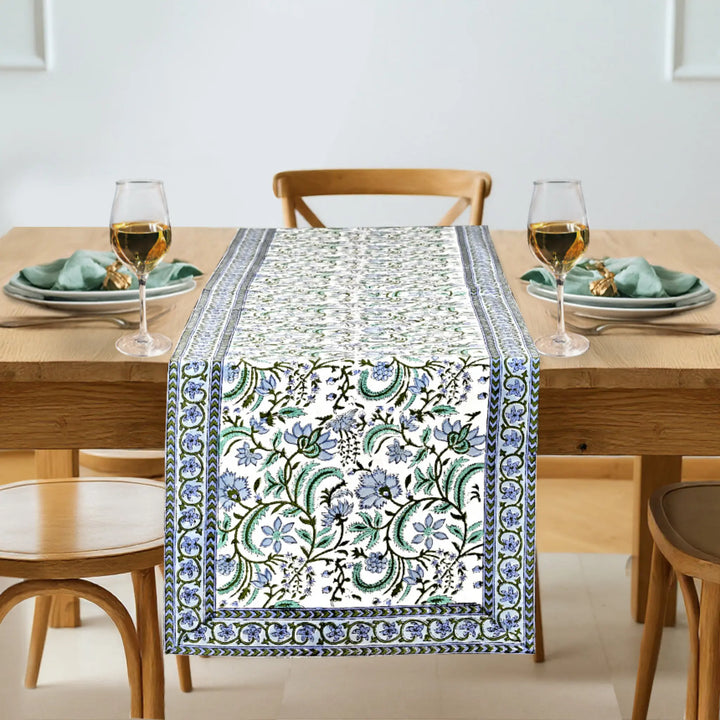 Dining table set with a floral patterned table runner, glasses, and plates.