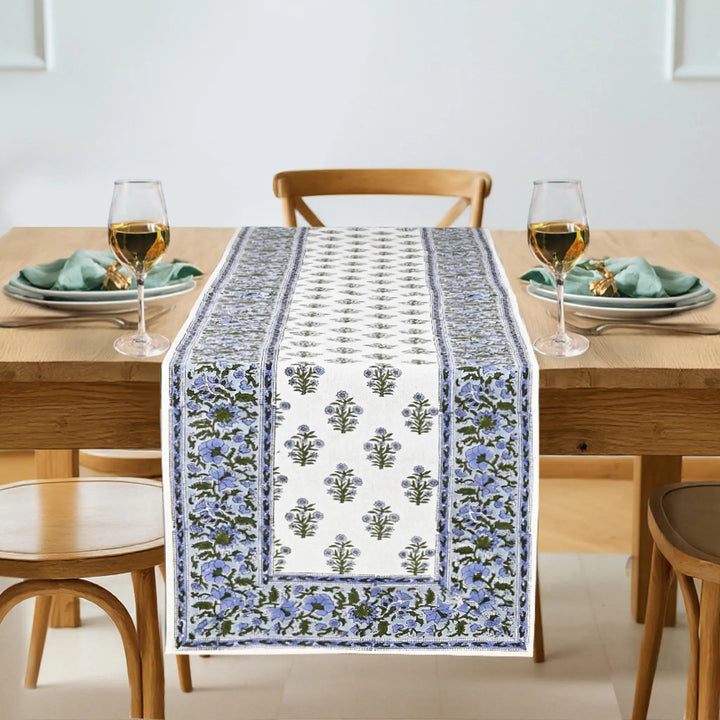 Dining table with a floral patterned table runner, glasses, and plates.
