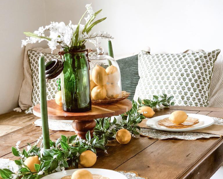Decorative table setting with greenery, candles, and fruit on a wooden table.