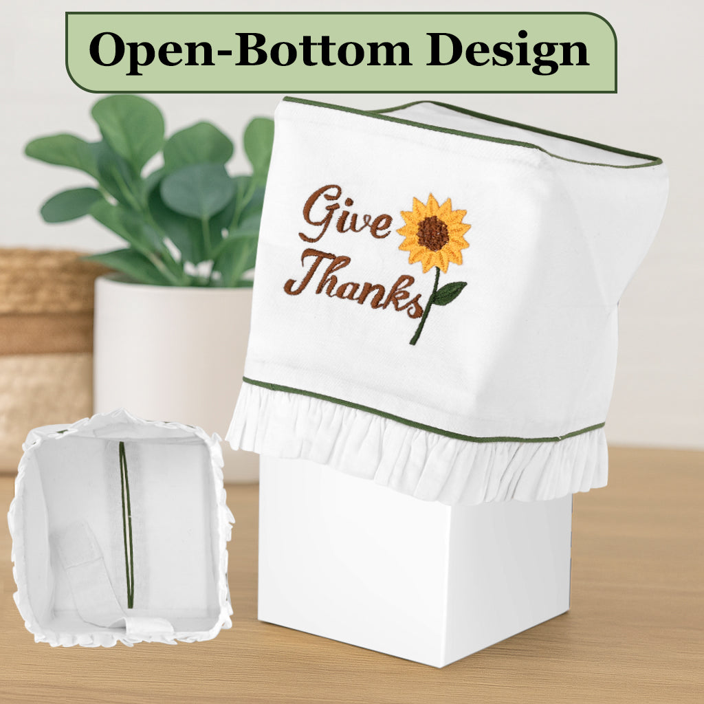 White dishcloth with 'Give Thanks' and sunflower design on a wooden surface with a plant in the background.