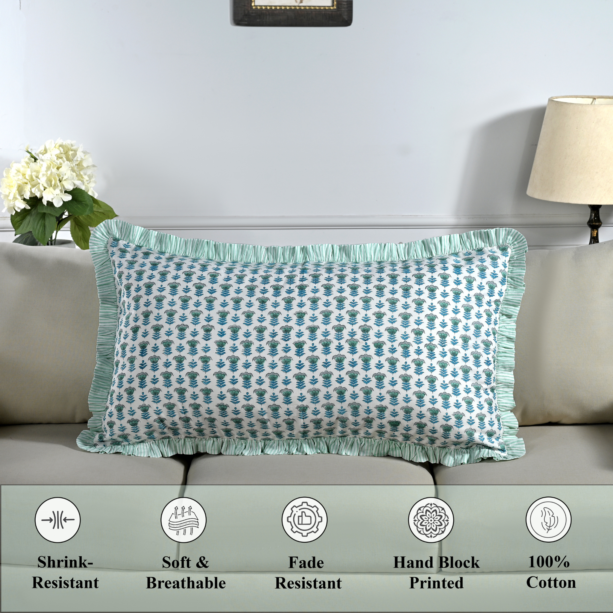 Cotton block print pillow cover placed on a bed with lamp and flowers in background.