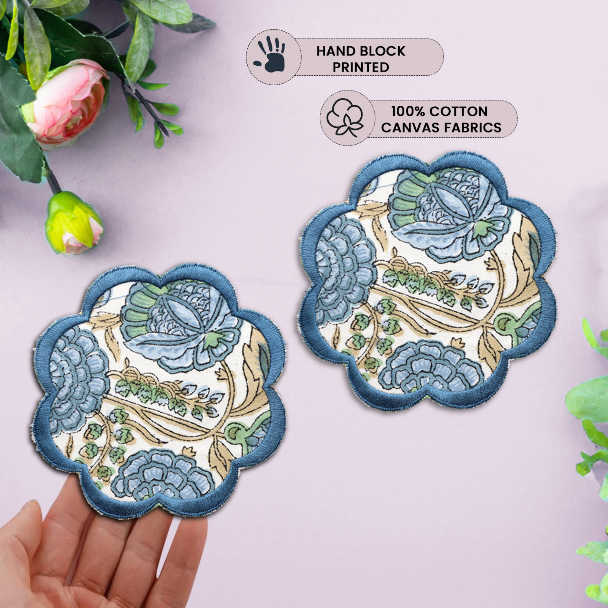Decorative fabric patches with floral designs held by a hand, surrounded by green leaves.