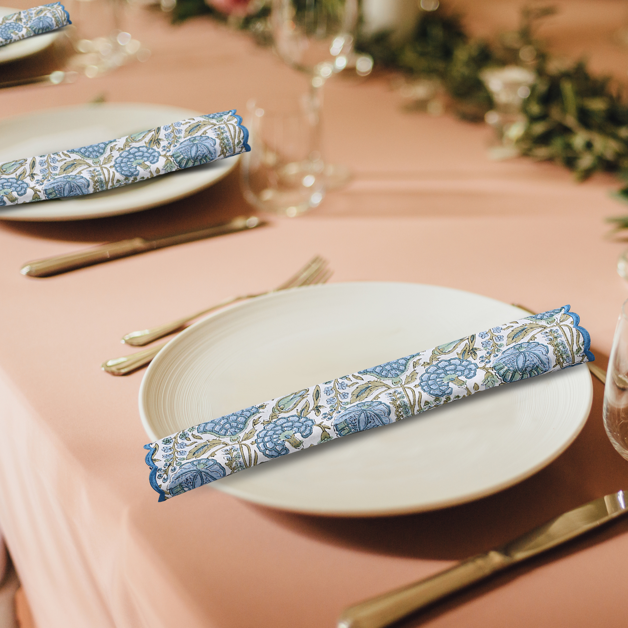 Table setting with floral-patterned napkins on plates against a pink tablecloth.