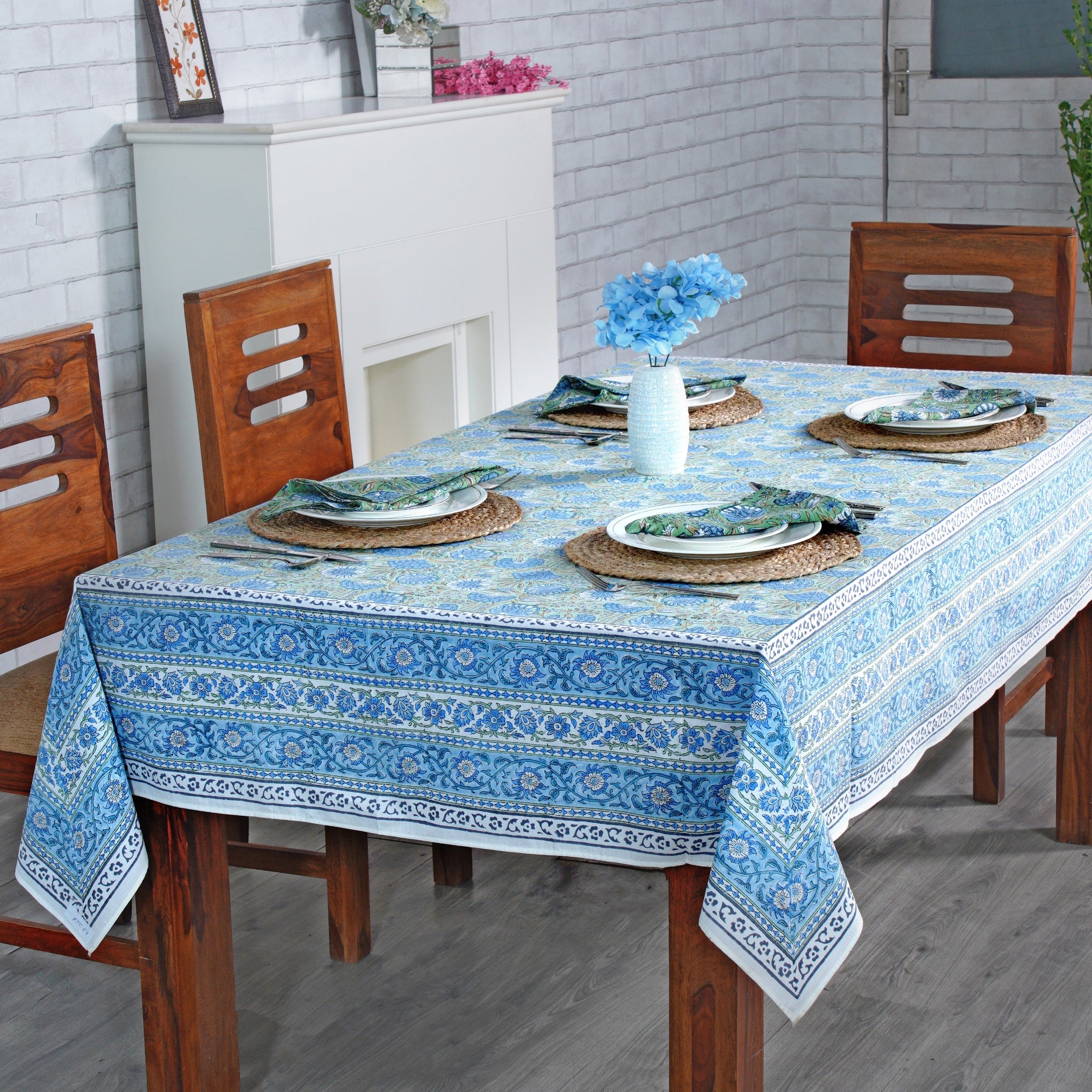 Dining table set with a blue patterned tablecloth, wooden chairs, and decorative items.