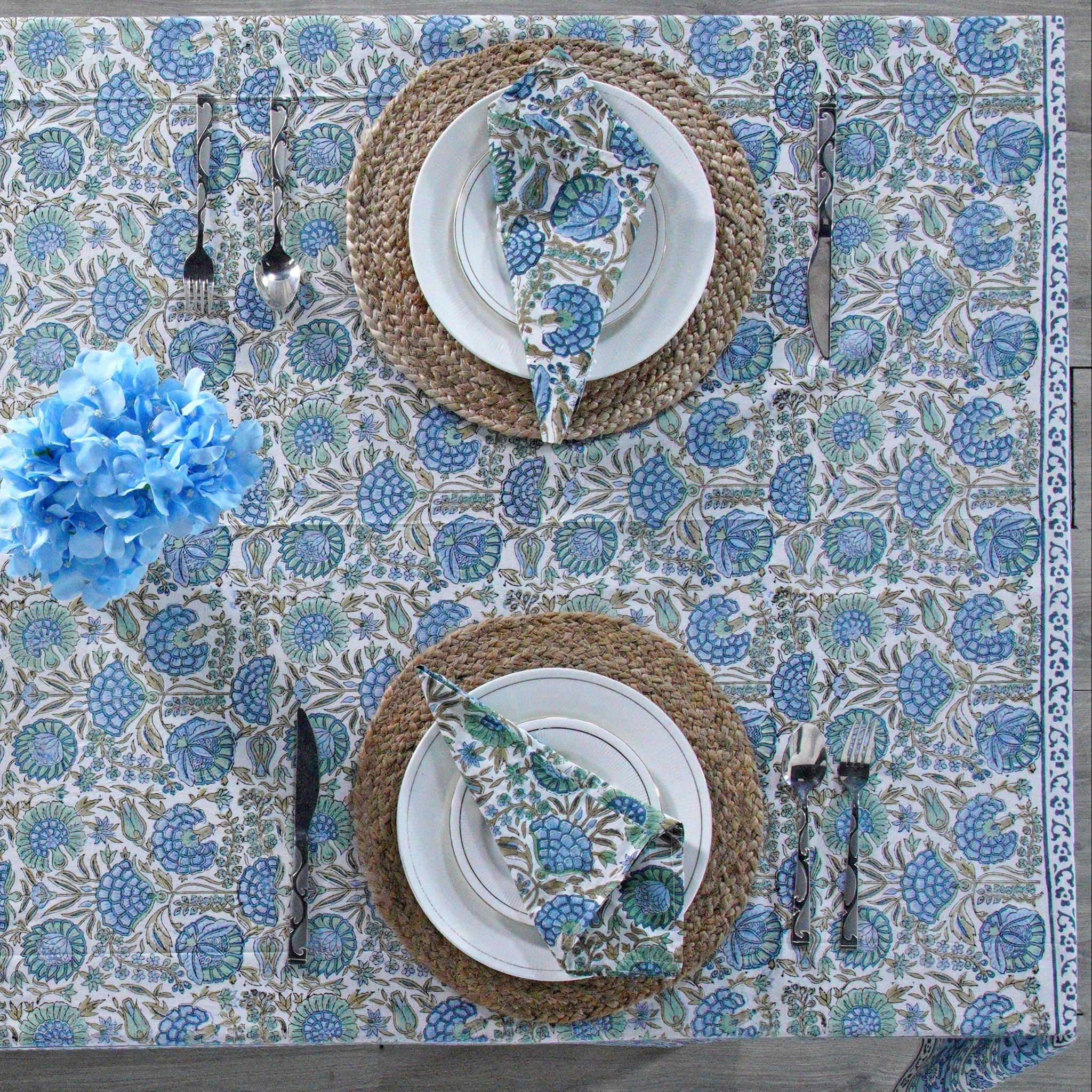 Table setting with floral tablecloth, plates, and cutlery on a decorative table.