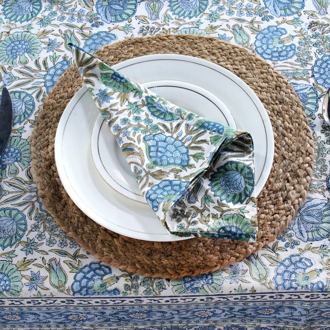 Table setting with white plates, napkin, and cutlery on a textured placemat over a patterned tablecloth.