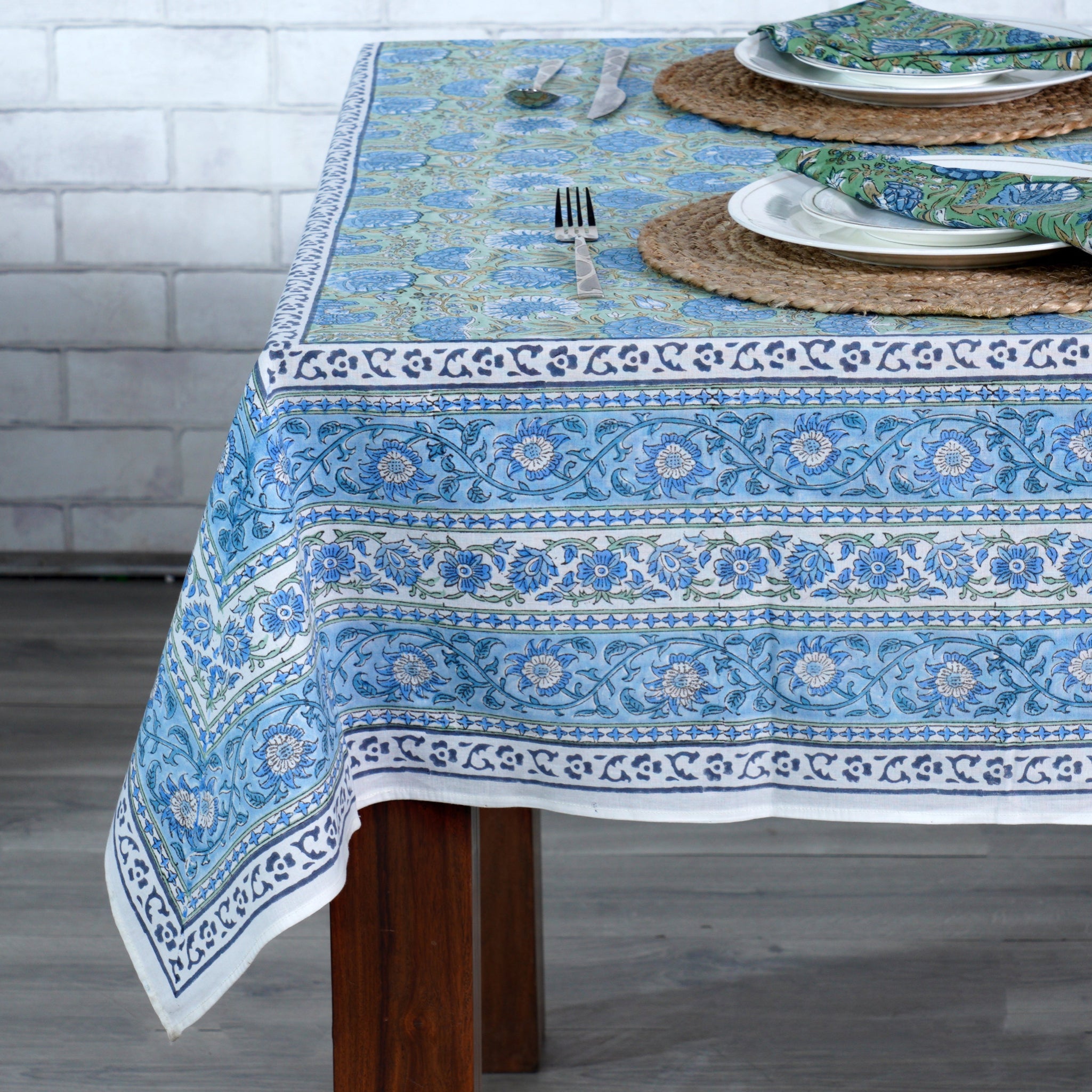 Table set with a blue patterned tablecloth in a room with a white brick wall.