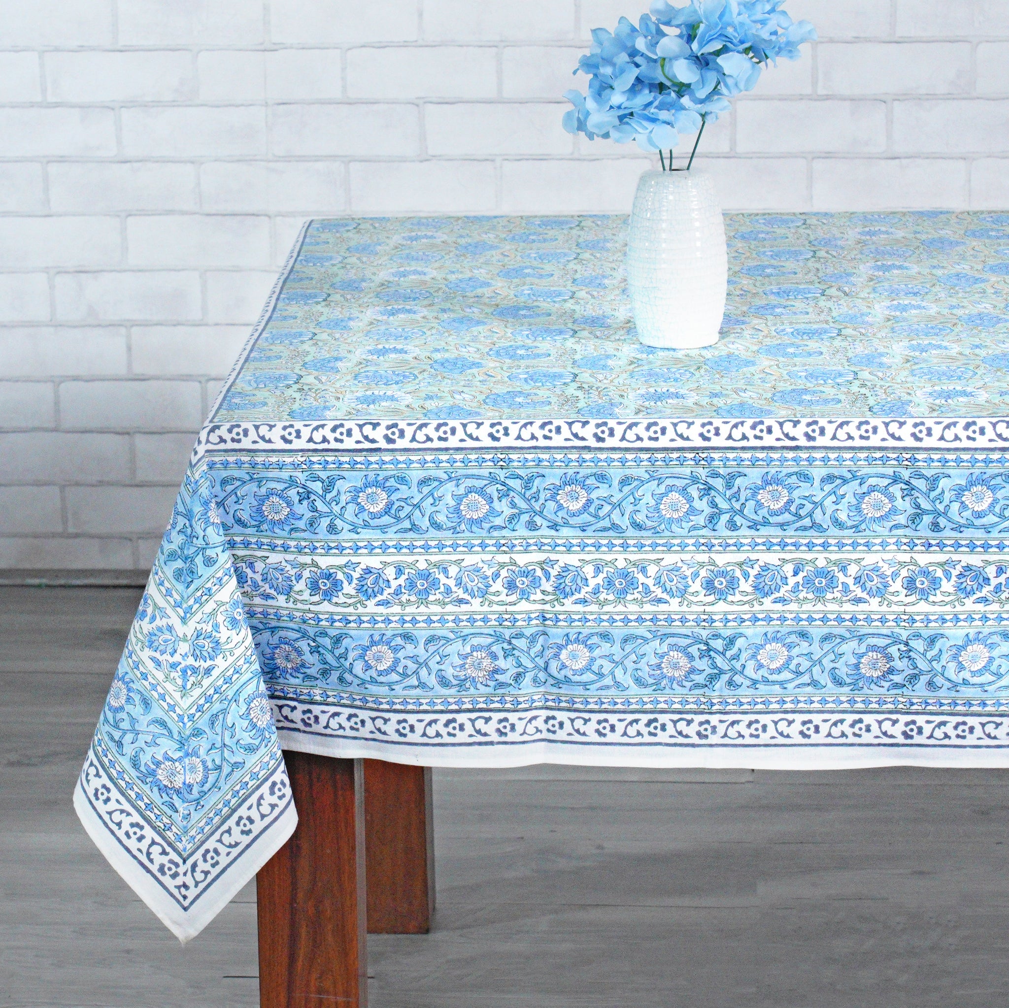 Tablecloth with blue and white pattern on a wooden table against a gray wall.