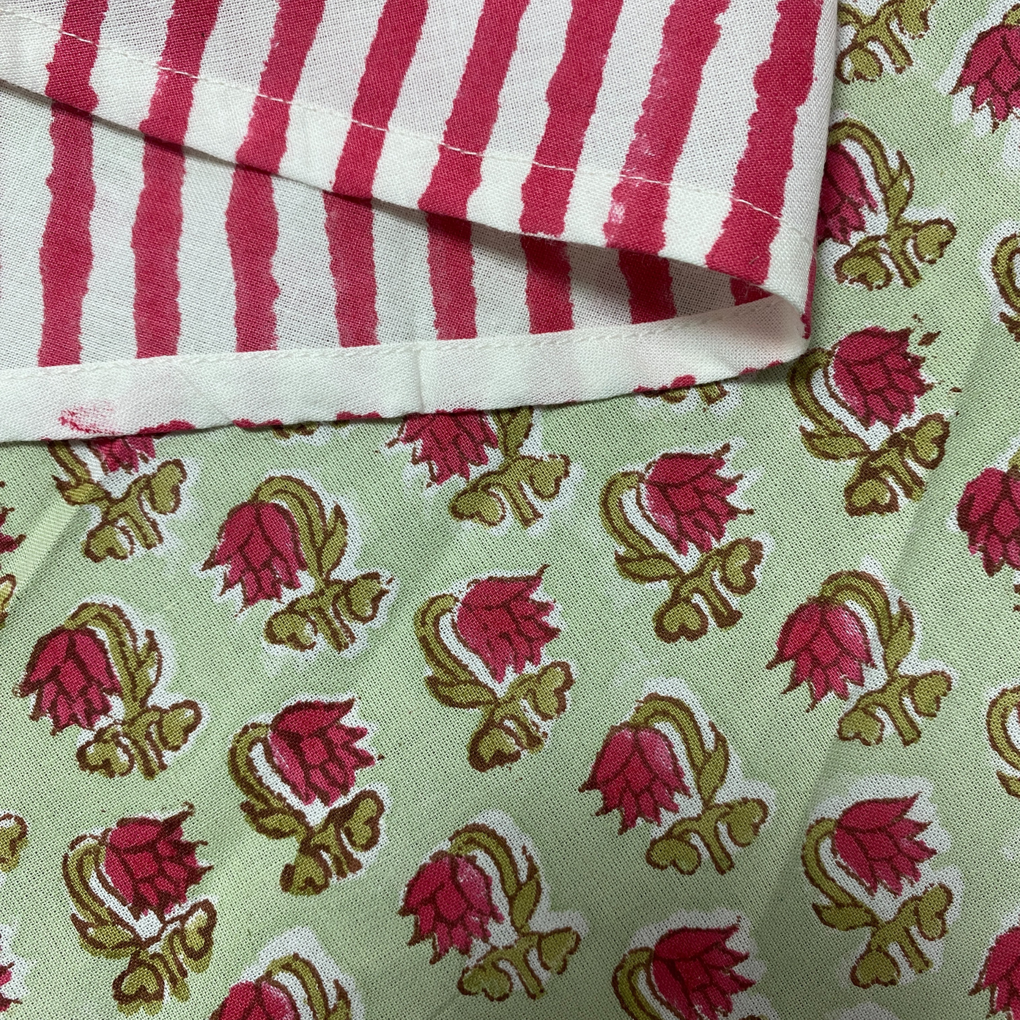 Close-up of fabric with red and white striped pattern on top and pink floral design on green background below.