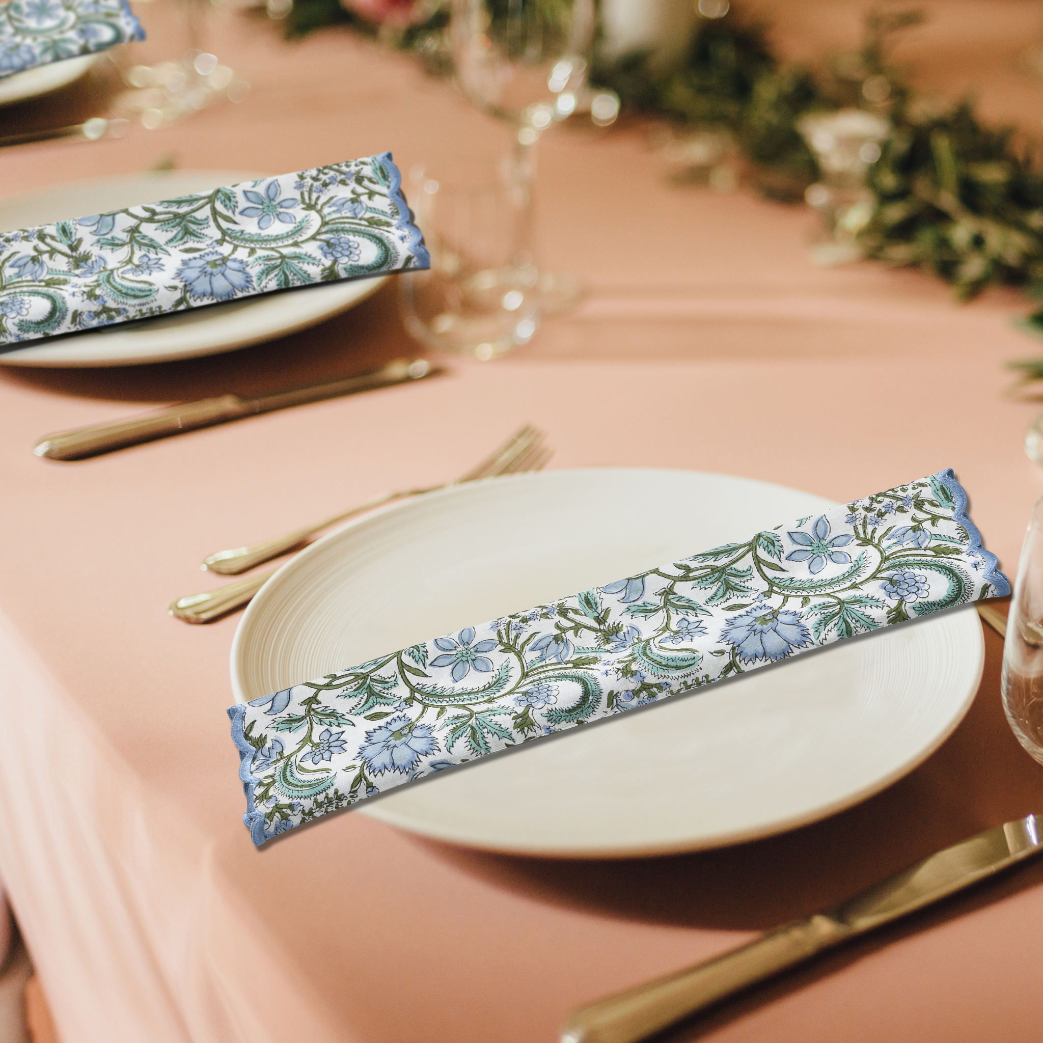 Decorative floral napkins on a table setting with pink tablecloth and greenery.