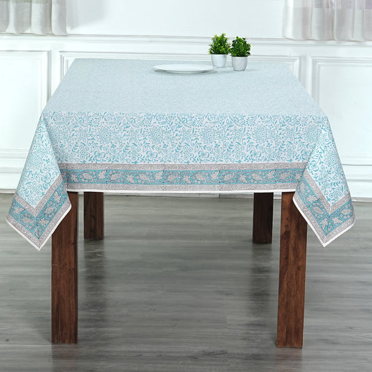 Tablecloth with floral pattern on a wooden table in a room with white walls and gray floor.
