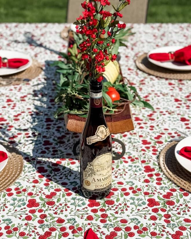 Decorative table setting with floral tablecloth, red napkins, and a bottle of wine.