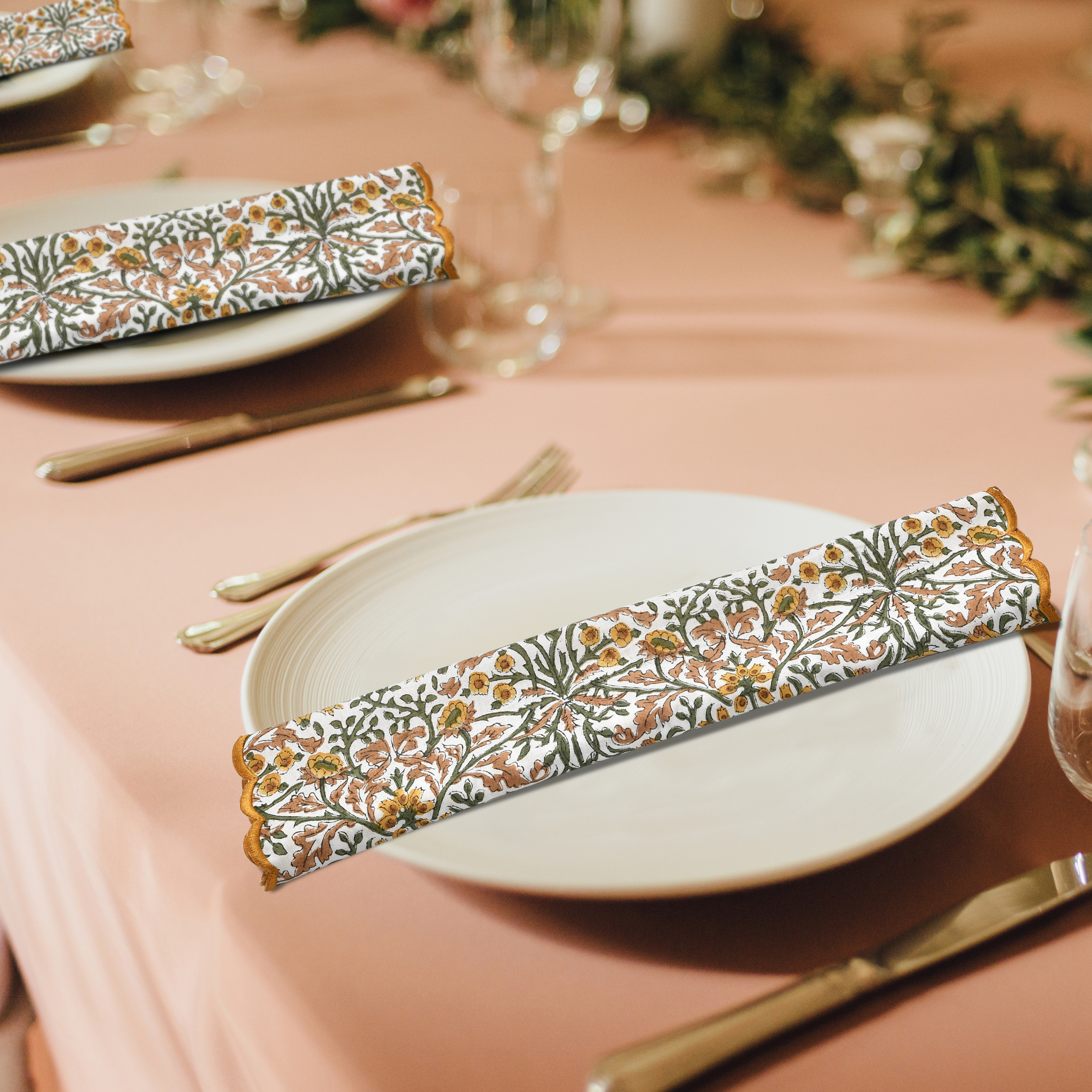 Decorative floral-patterned napkin on a plate with a pink tablecloth and greenery.