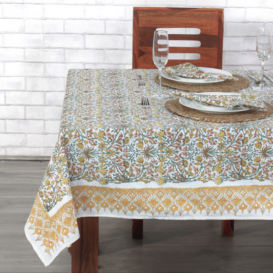 Dining table set with a floral patterned tablecloth against a white brick wall.