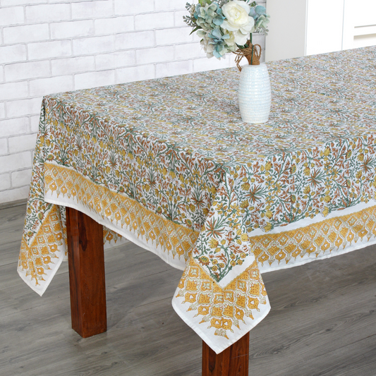 Tablecloth with floral pattern on a wooden table against a white brick wall.