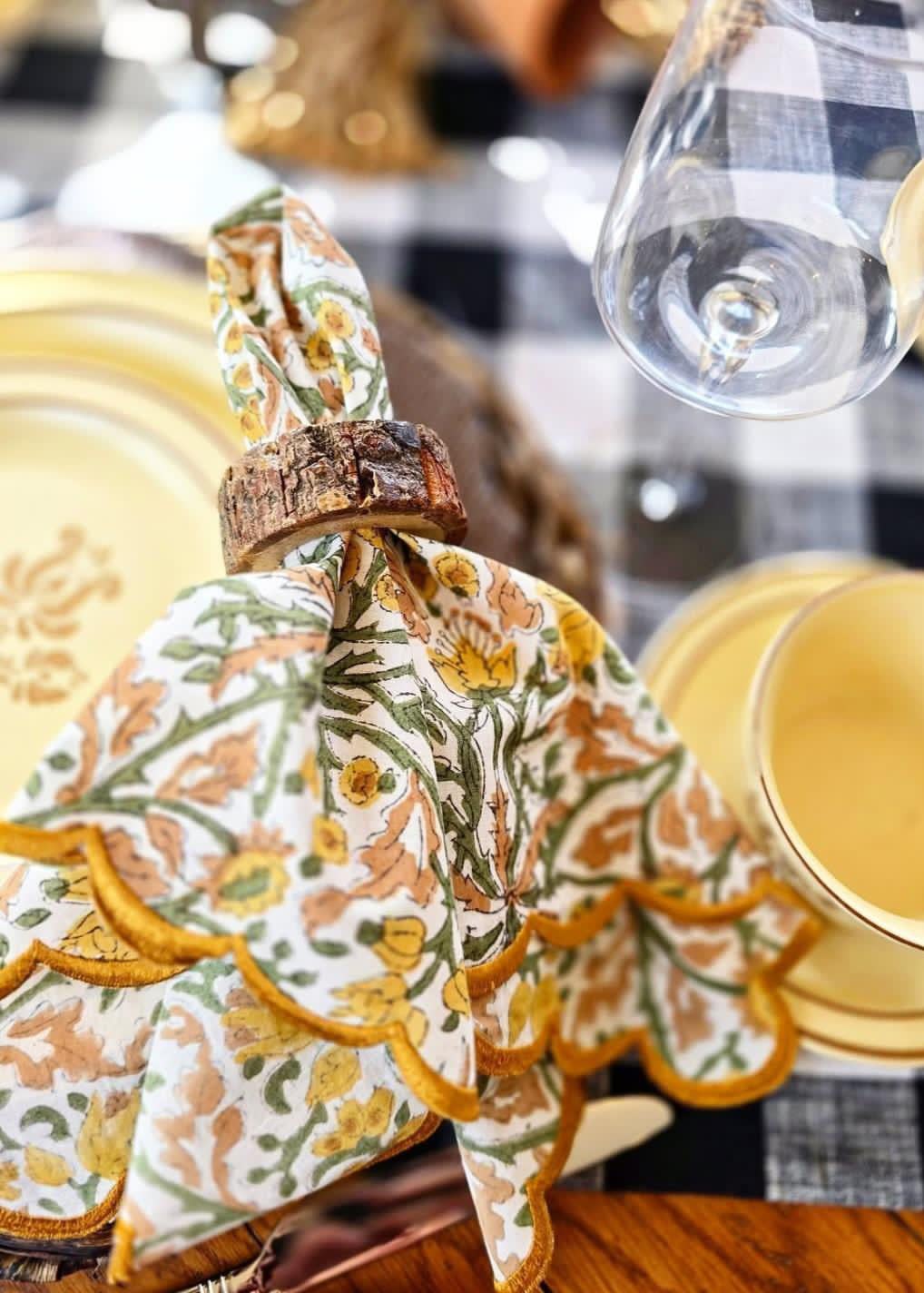 Decorative napkin with floral pattern on a table setting with gold plates and checkered tablecloth.