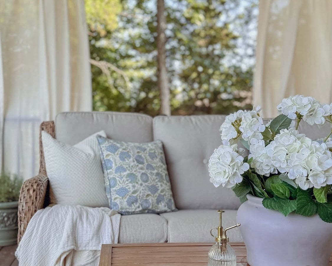 Outdoor living space with a gray sofa, decorative pillows, and a vase of white flowers.