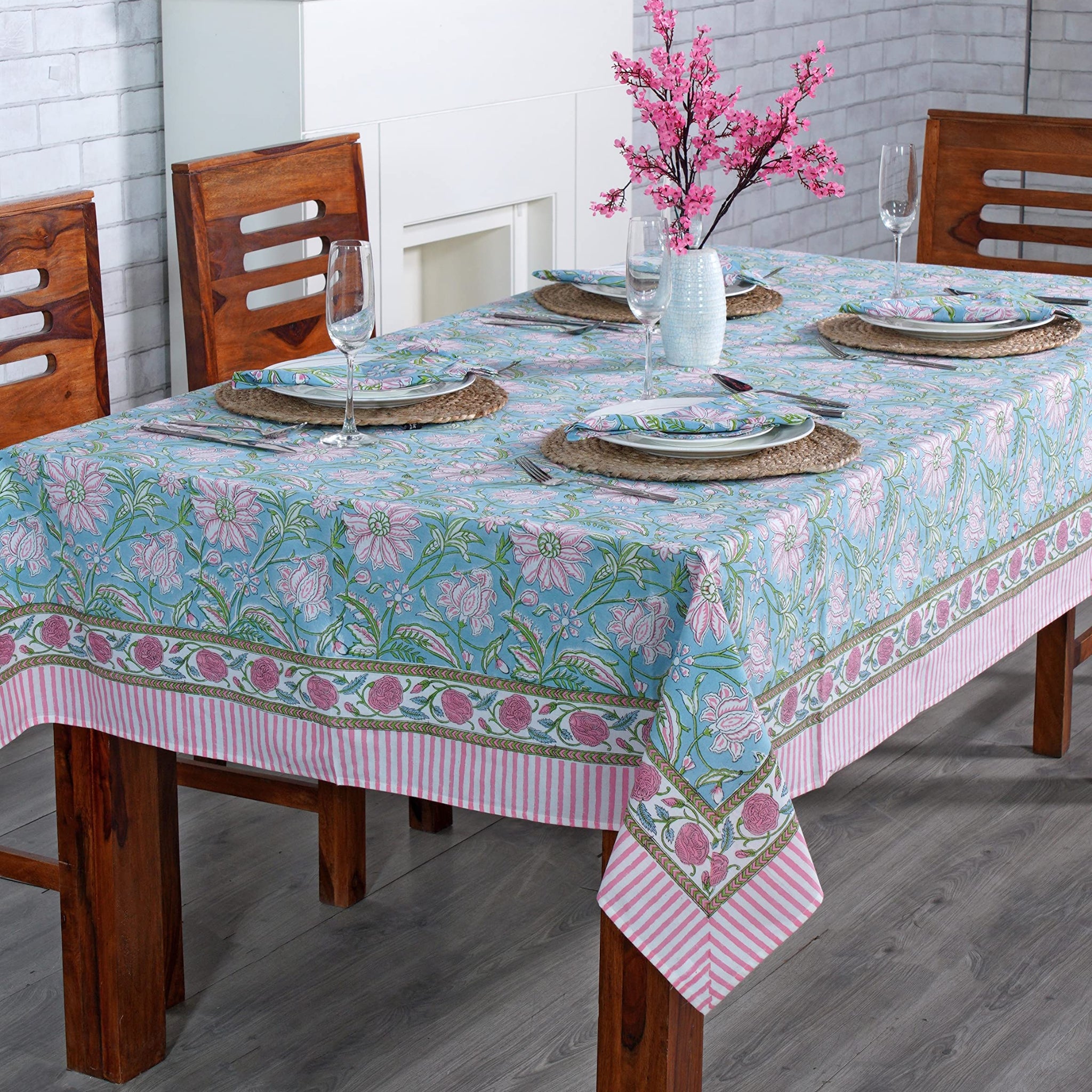 Dining table set with a floral tablecloth in a room with wooden chairs and a fireplace.