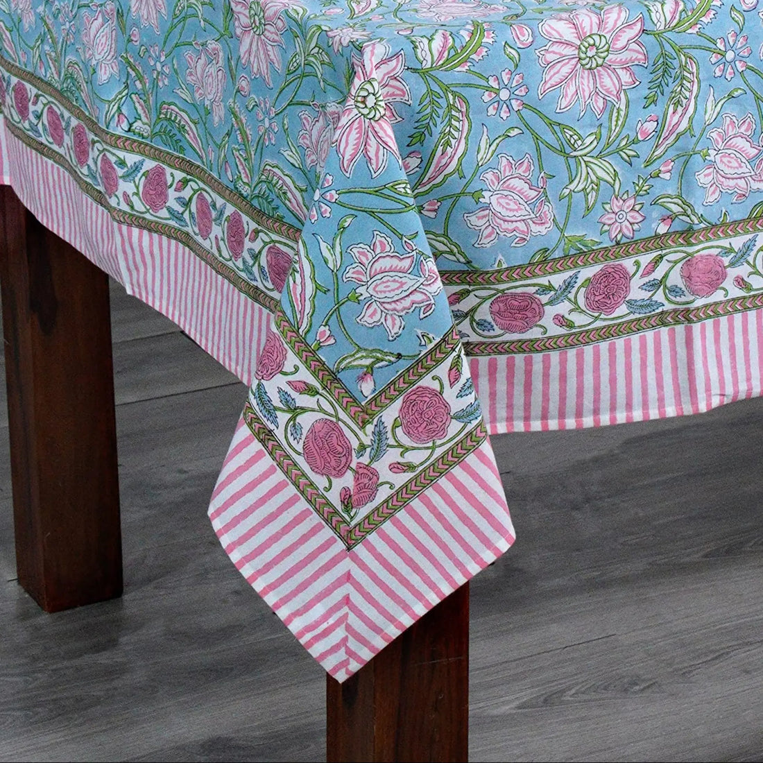 Tablecloth with floral pattern on a wooden table against a white brick wall.