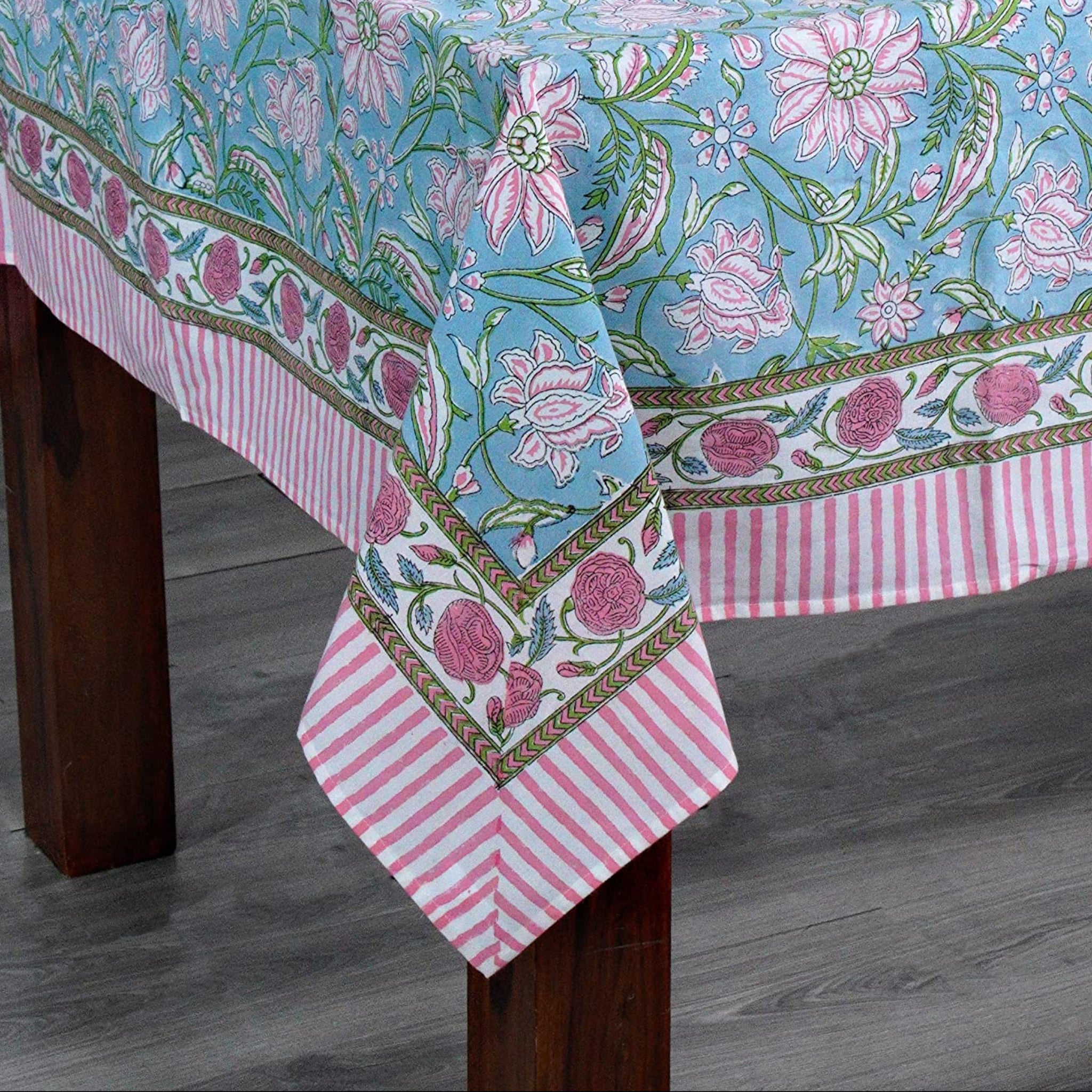 Tablecloth with floral pattern on a wooden table against a white brick wall.