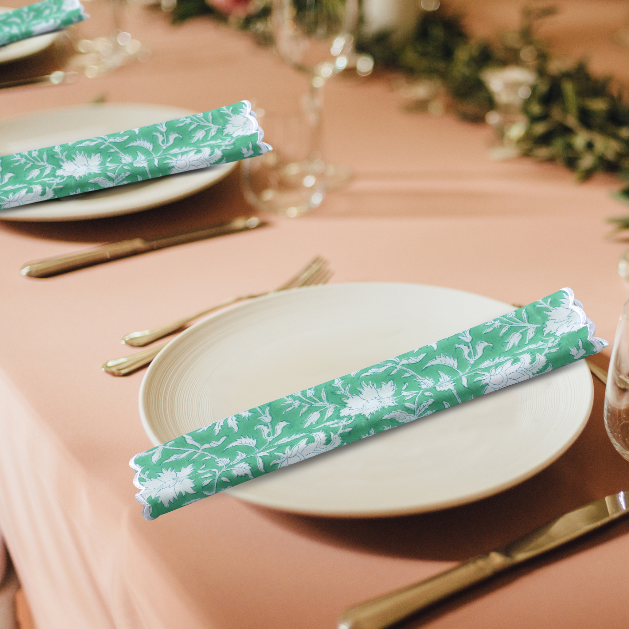 Table setting with green floral-patterned napkins on a pink tablecloth.