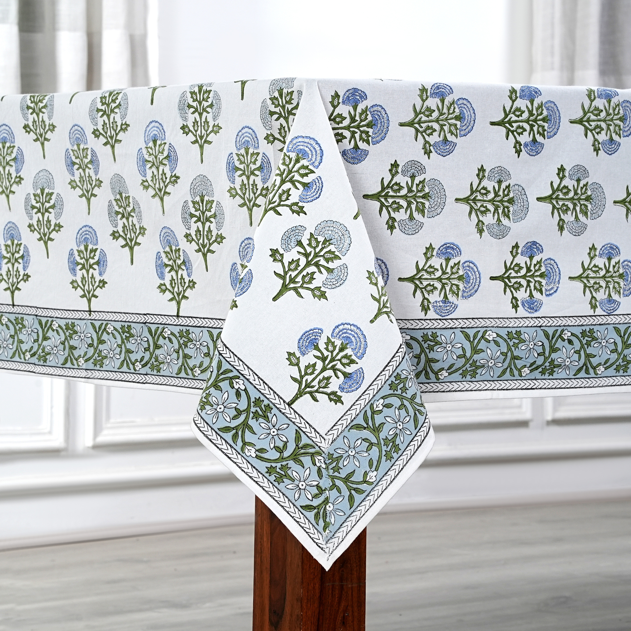 Floral patterned tablecloth on a wooden table with a white curtain background