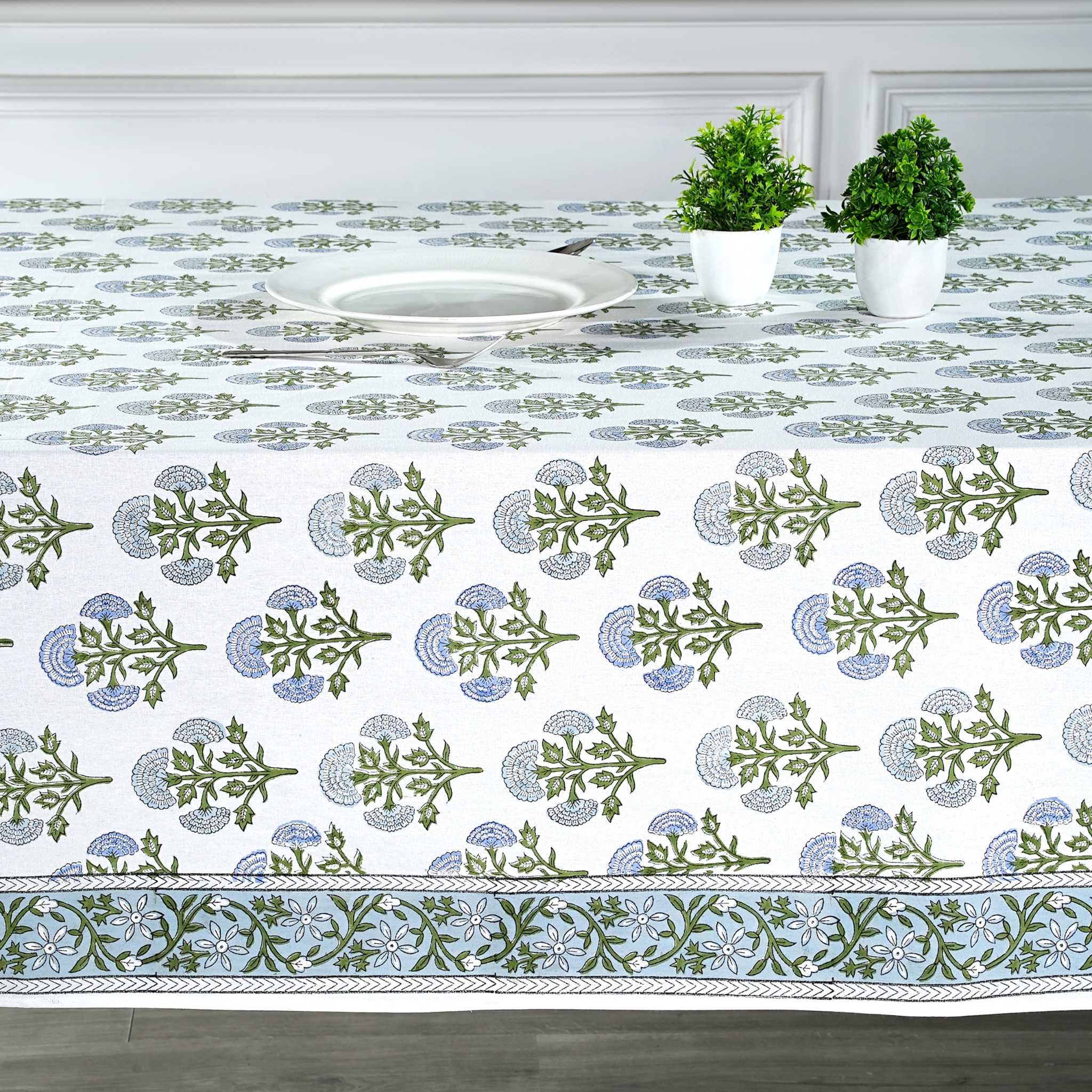 Decorative tablecloth with green and blue patterns on a table set with plates and plants.