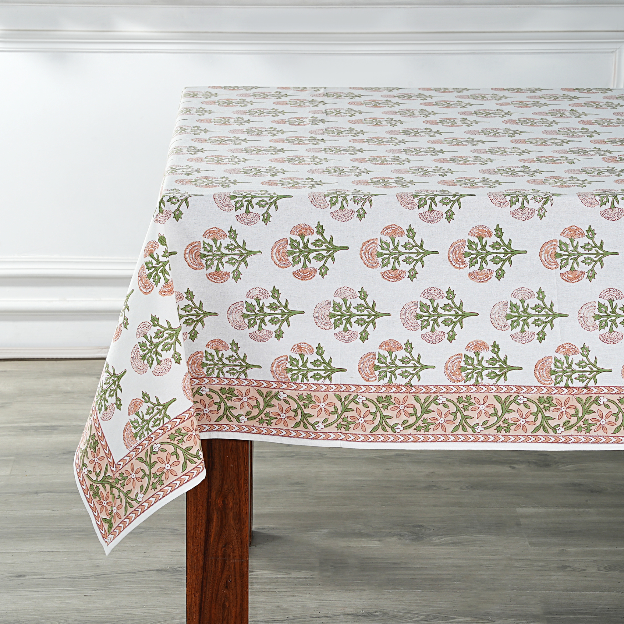 Tablecloth with floral pattern on a wooden table against a white wall.