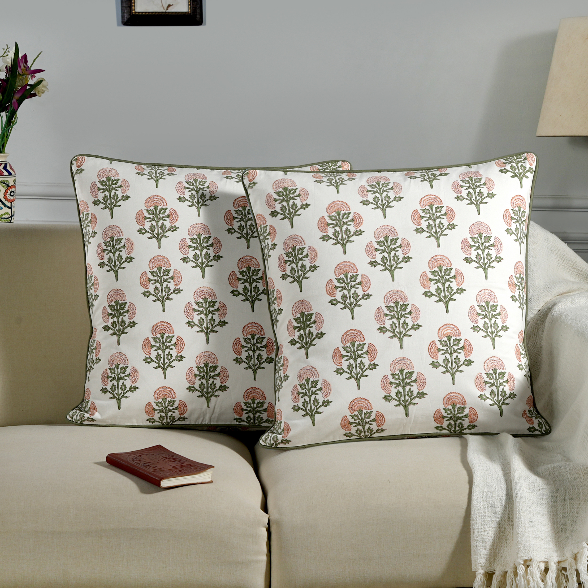 Decorative pillows with floral pattern on a beige sofa with a book and flowers in the background.