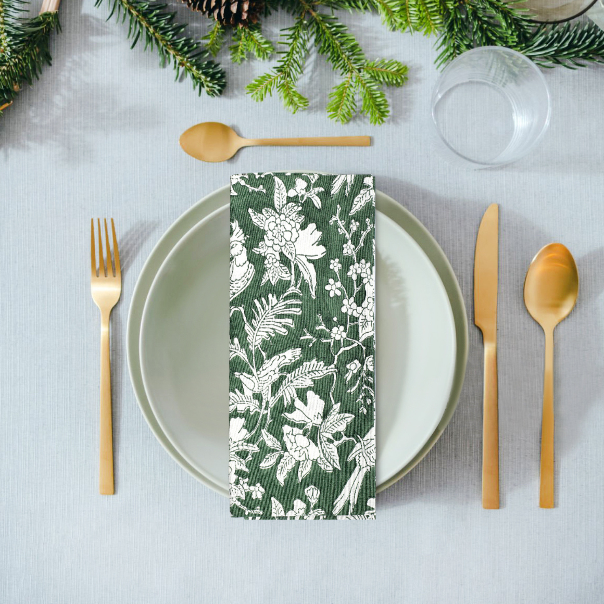 Table setting with a floral-patterned napkin on a white plate, surrounded by gold cutlery and greenery.