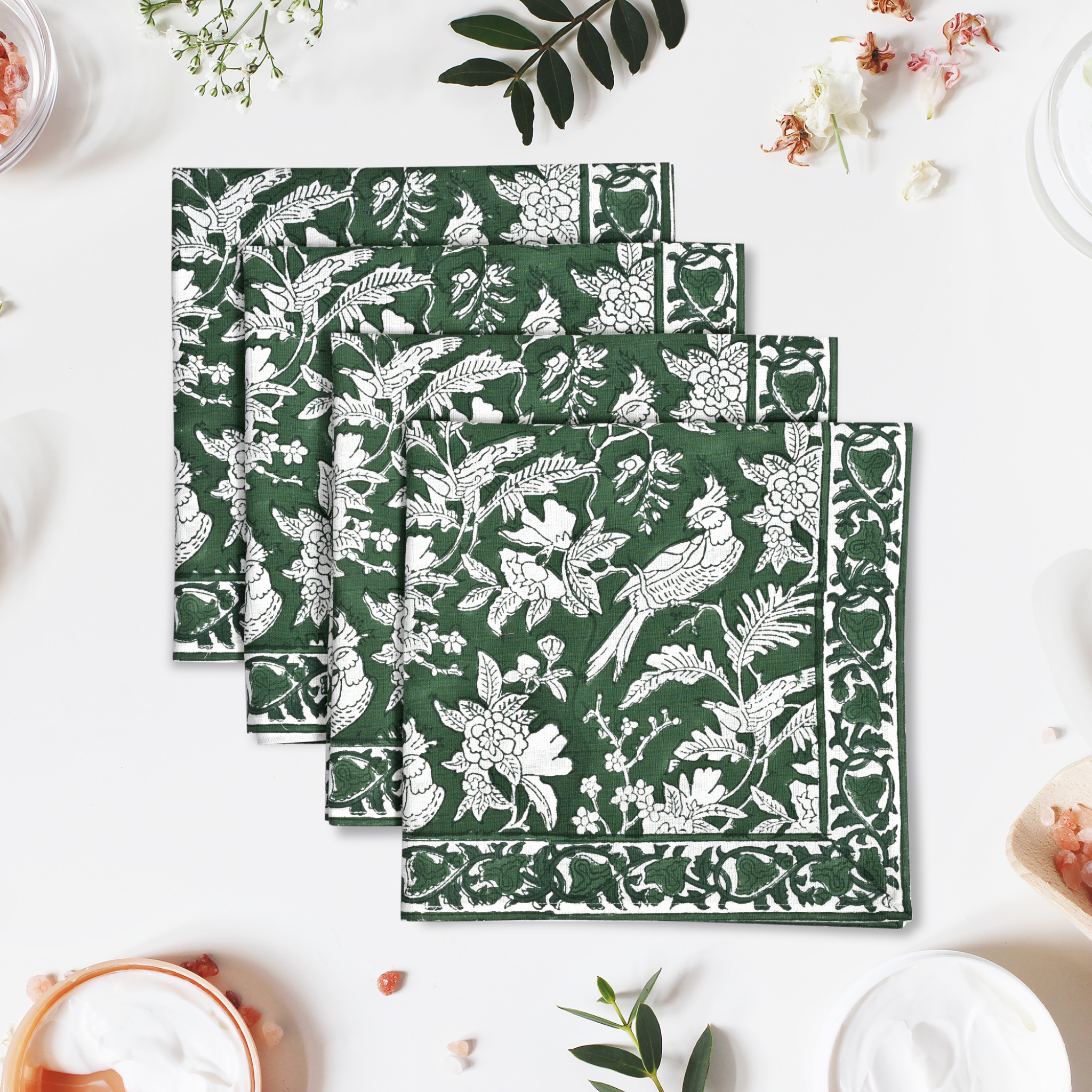 Set of three green napkins with white floral and bird pattern on a white surface.