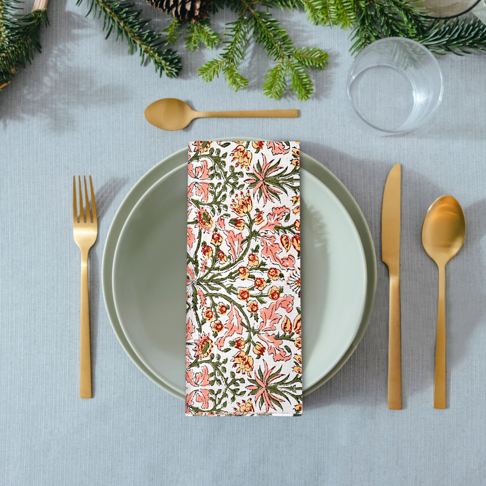 Decorative floral-patterned napkin on a table setting with gold cutlery and greenery.