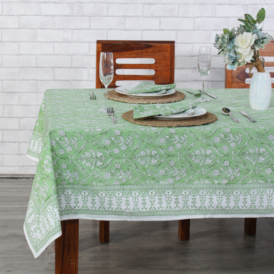 Dining table set with a green and white patterned tablecloth, wooden chairs, and white plates.