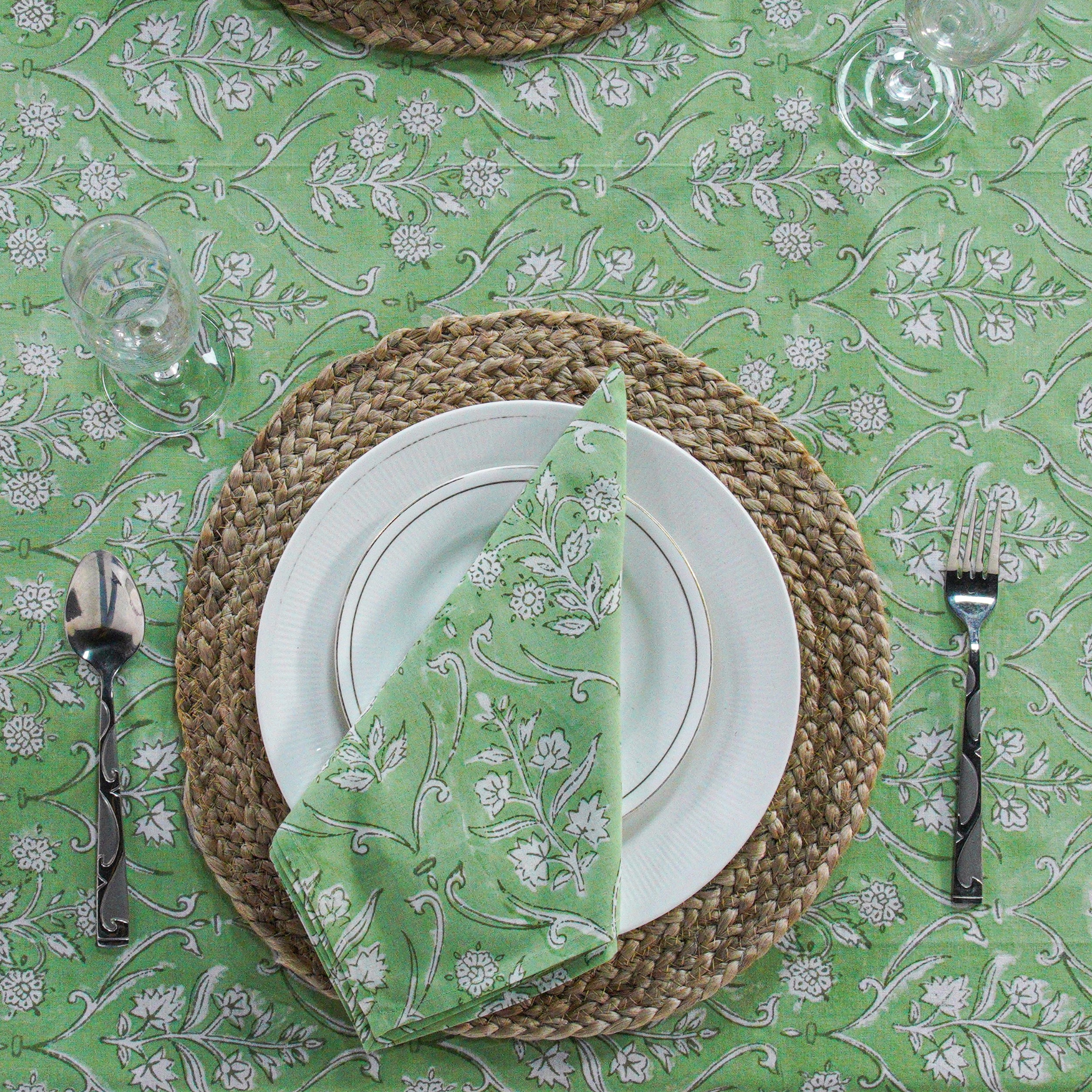 Dining table setting with green and white floral patterned tablecloth, plates, napkin, and cutlery.