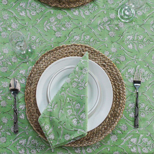 Dining table setting with green and white floral patterned tablecloth, plates, napkin, and cutlery.