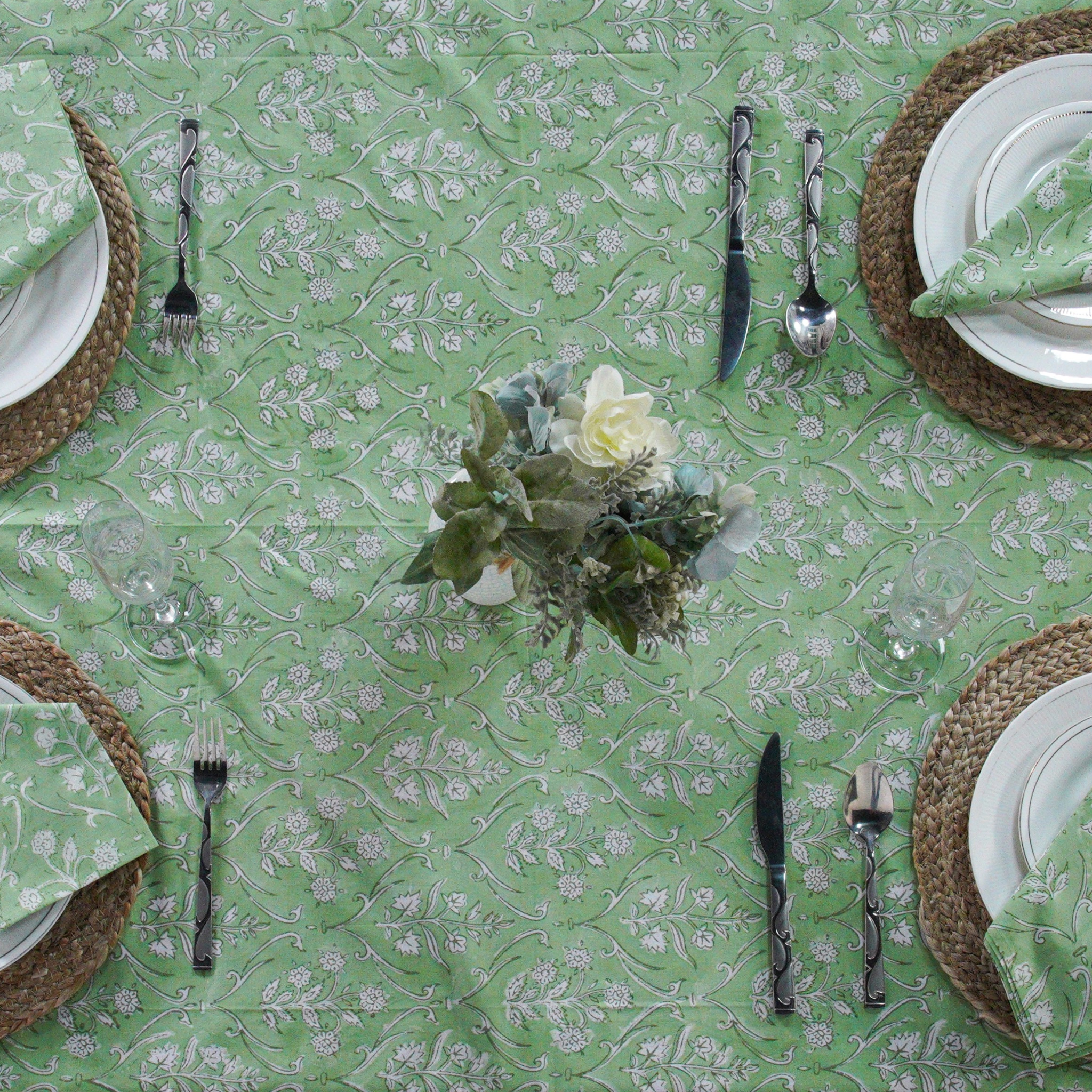 Green floral-patterned tablecloth with white plates, silverware, and woven placemats.