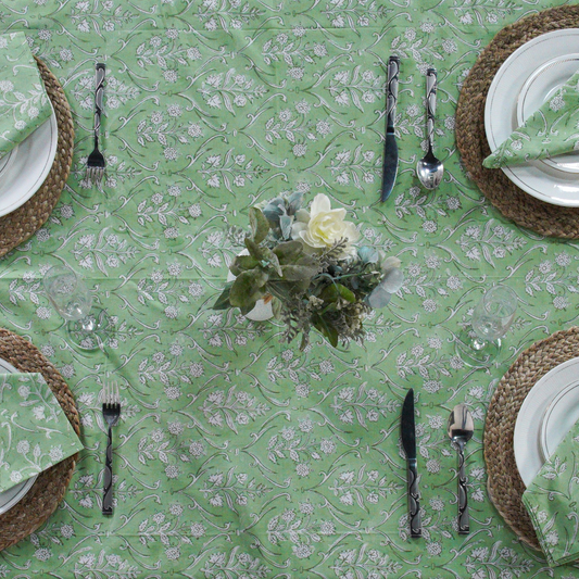 Green floral-patterned tablecloth with white plates, silverware, and woven placemats.