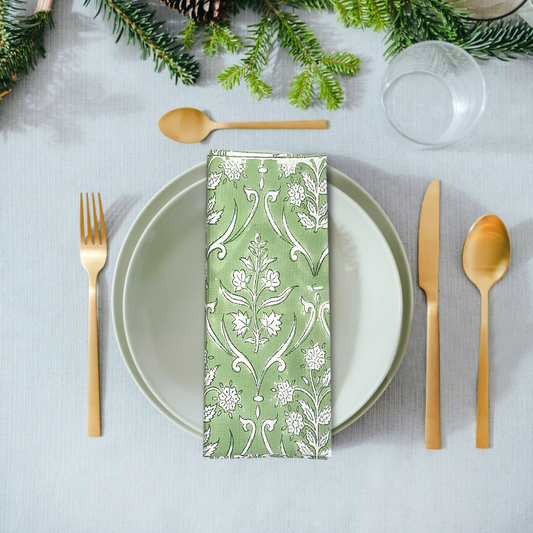 Table setting with a green patterned napkin, white plate, gold cutlery, and Christmas decorations.