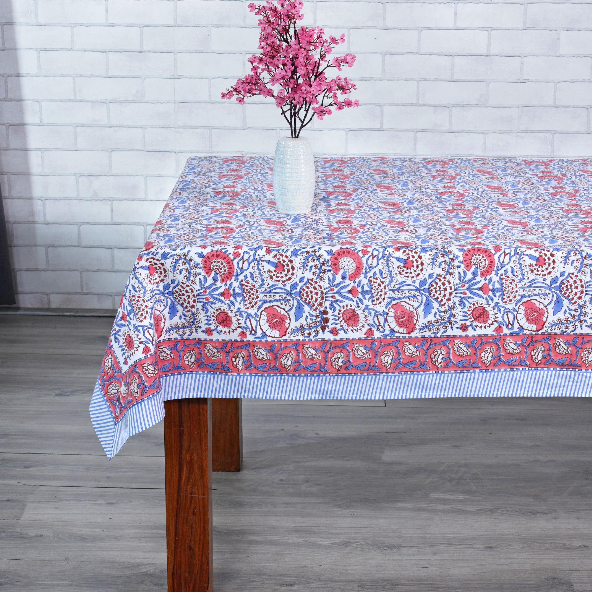 Tablecloth with floral pattern on a wooden table against a white brick wall.
