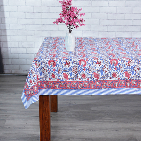 Tablecloth with floral pattern on a wooden table against a white brick wall.