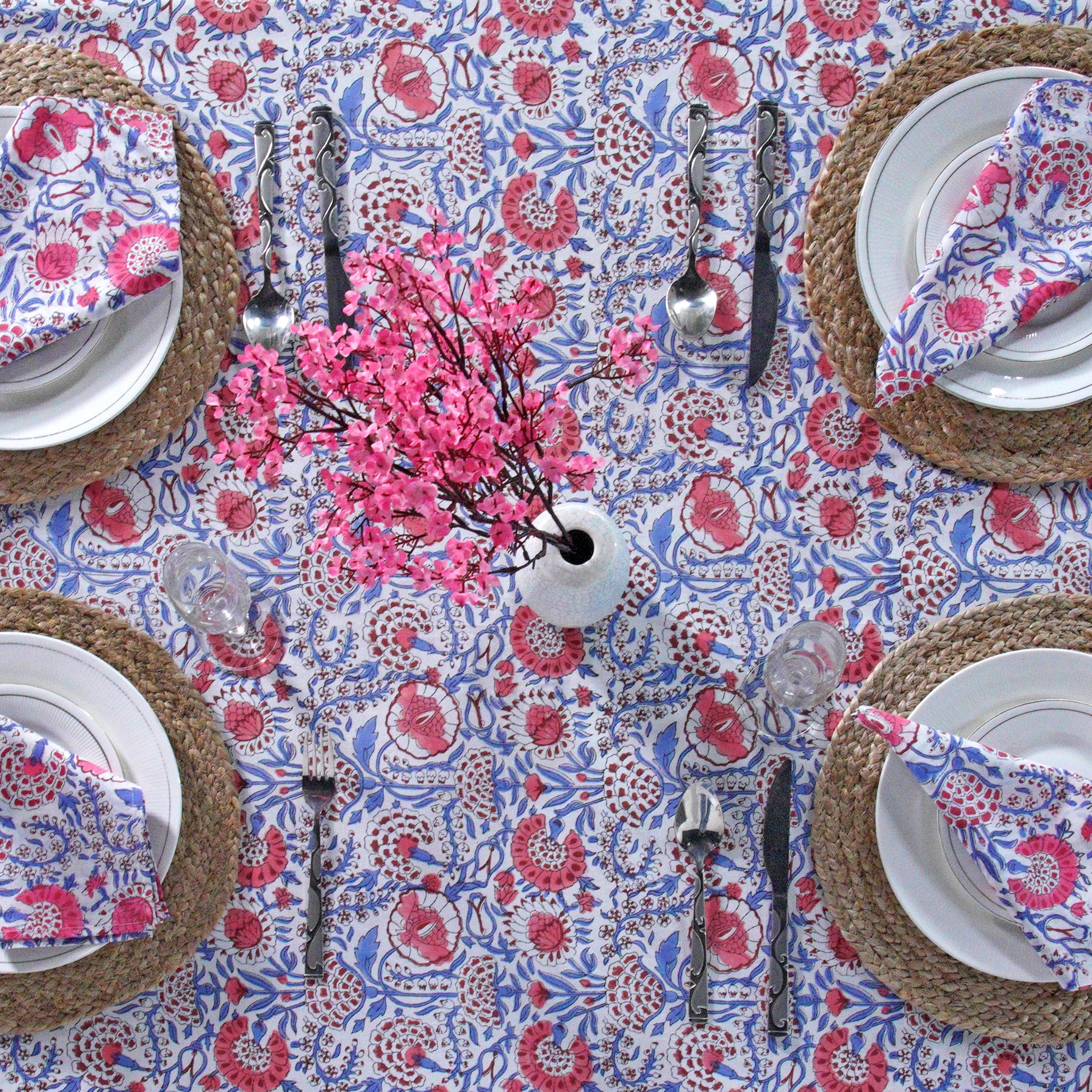 Table setting with floral tablecloth, plates, cutlery, and pink floral centerpieces.