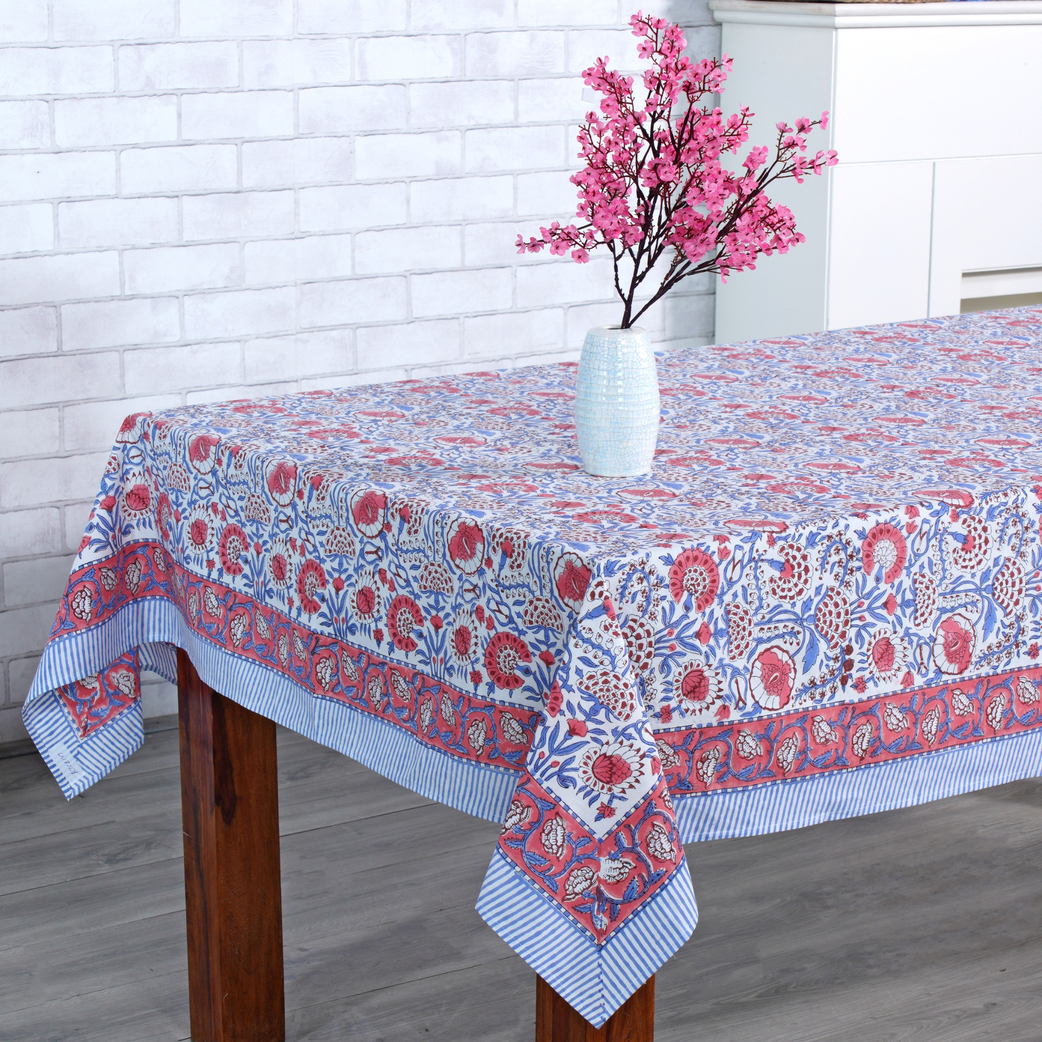 Tablecloth with floral pattern on a wooden table against a white brick wall.