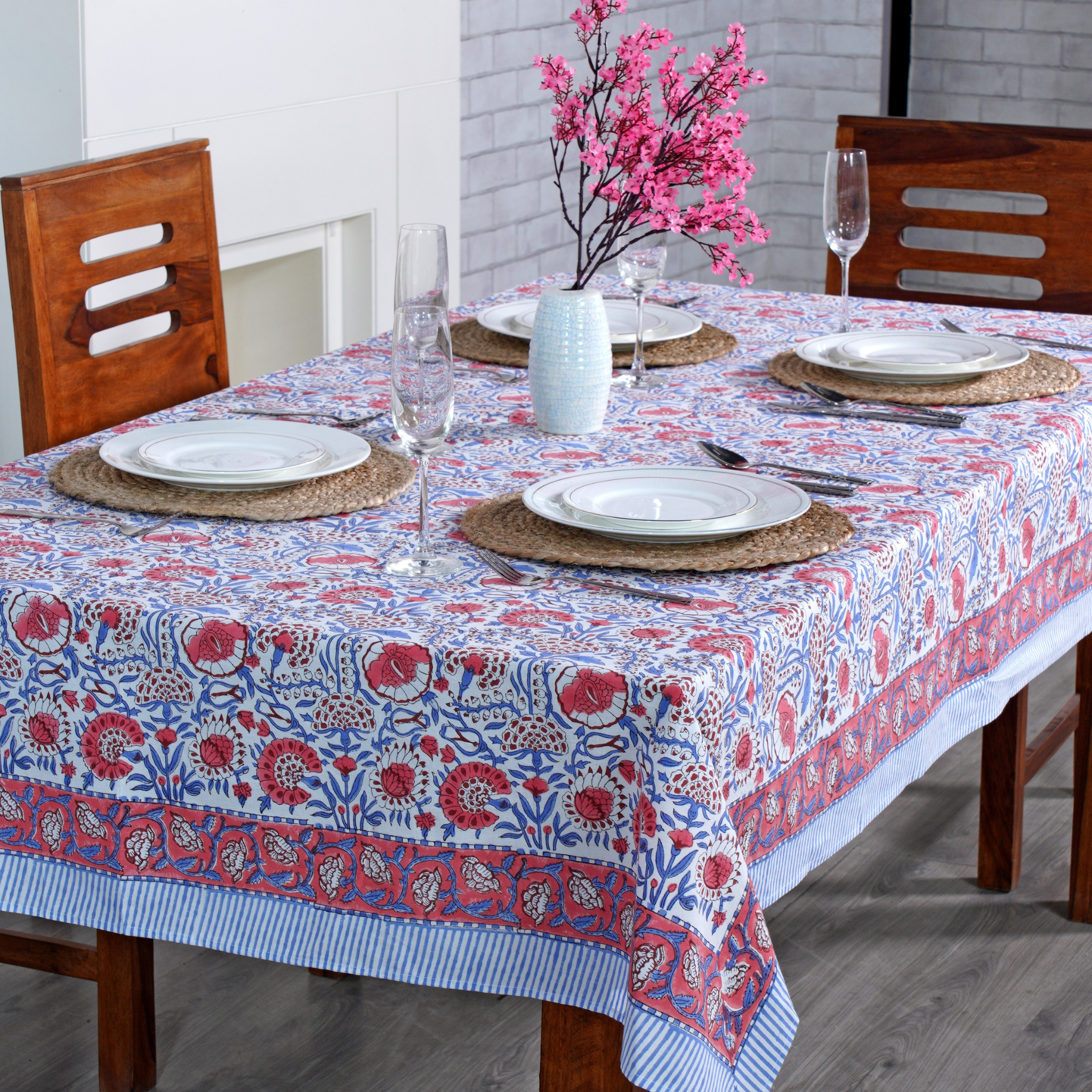 Dining table set with a floral patterned tablecloth, plates, glasses, and cutlery.
