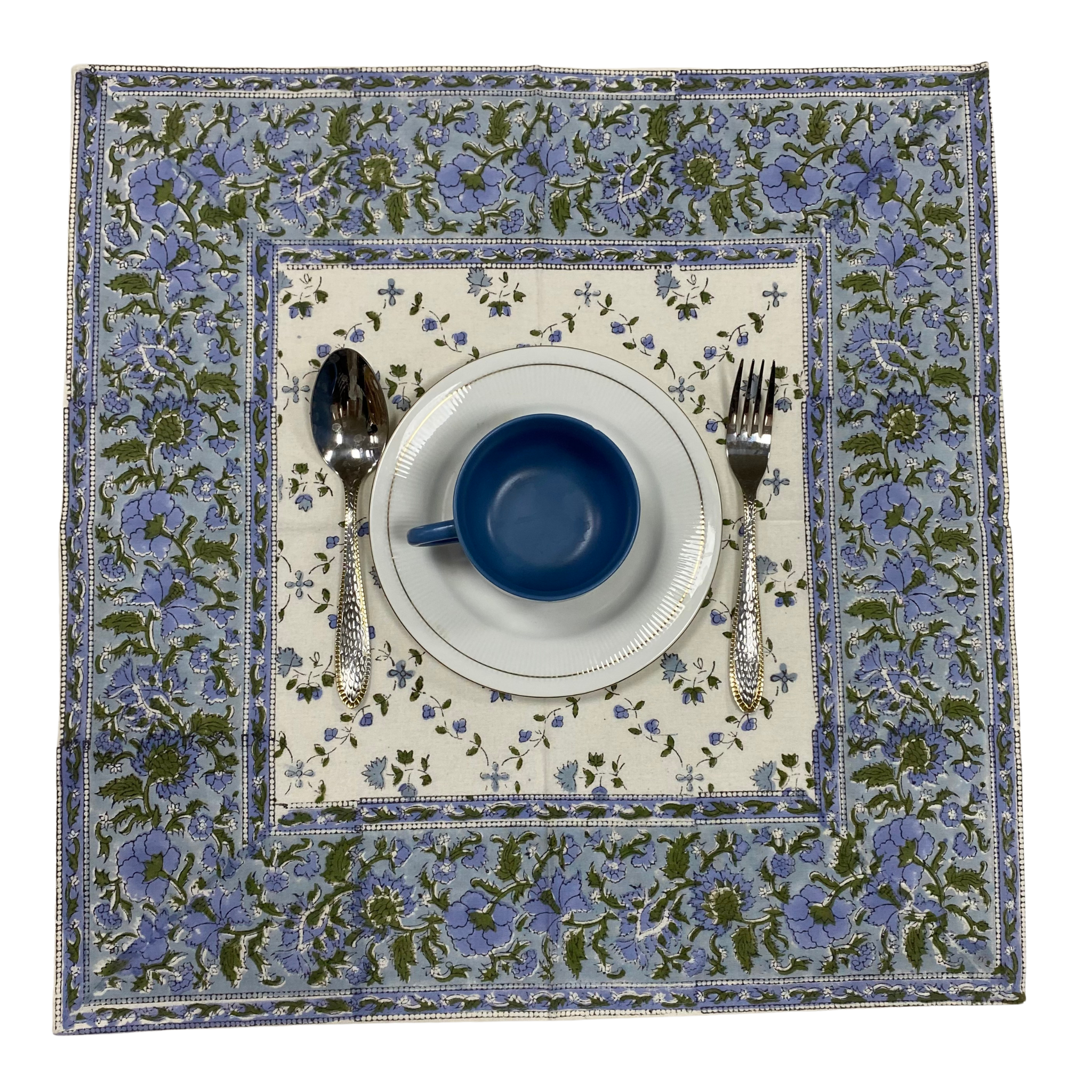 Placemat with floral pattern, blue cup and saucer, silver spoon and fork on a white background