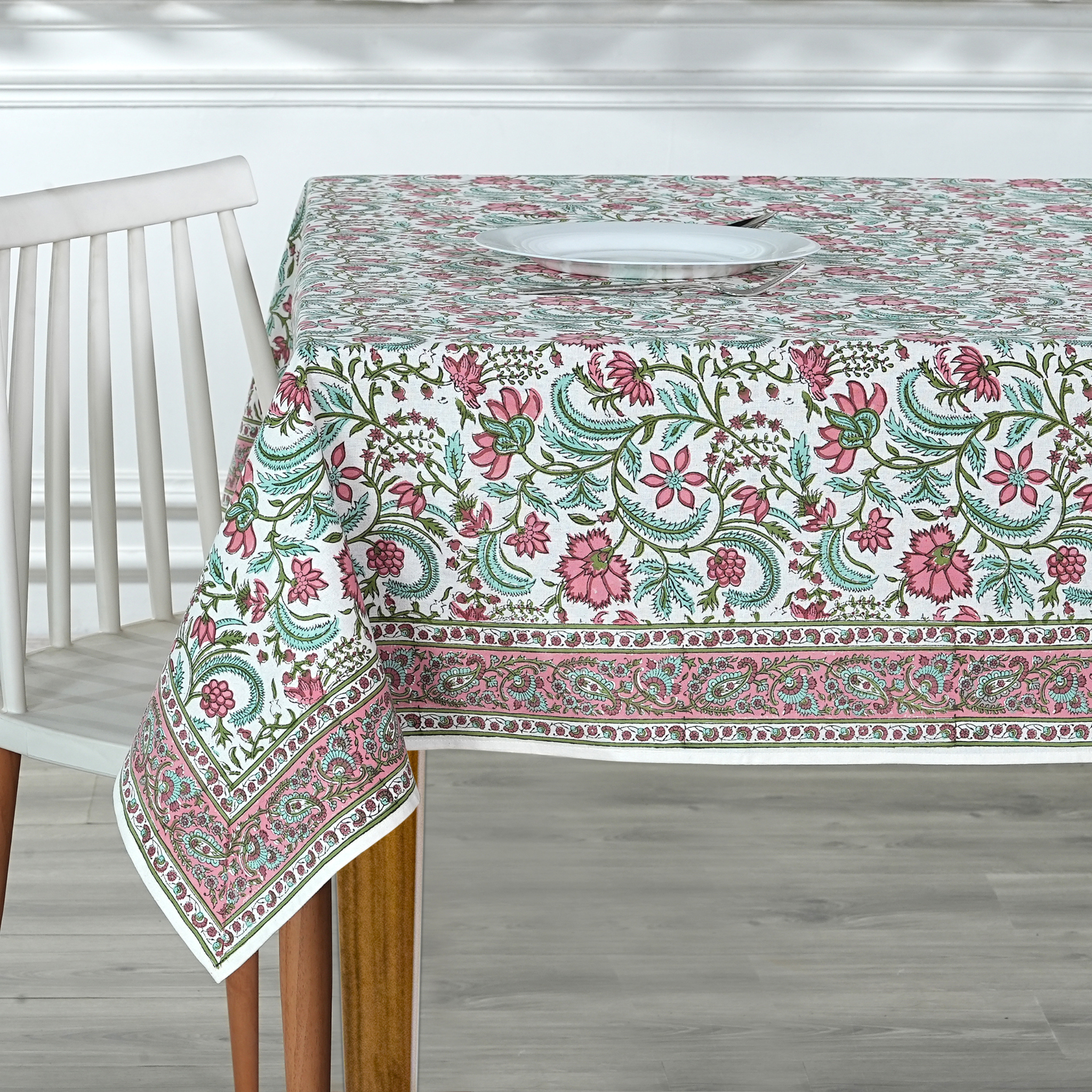 Floral patterned tablecloth on a wooden table with a chair in a room setting.