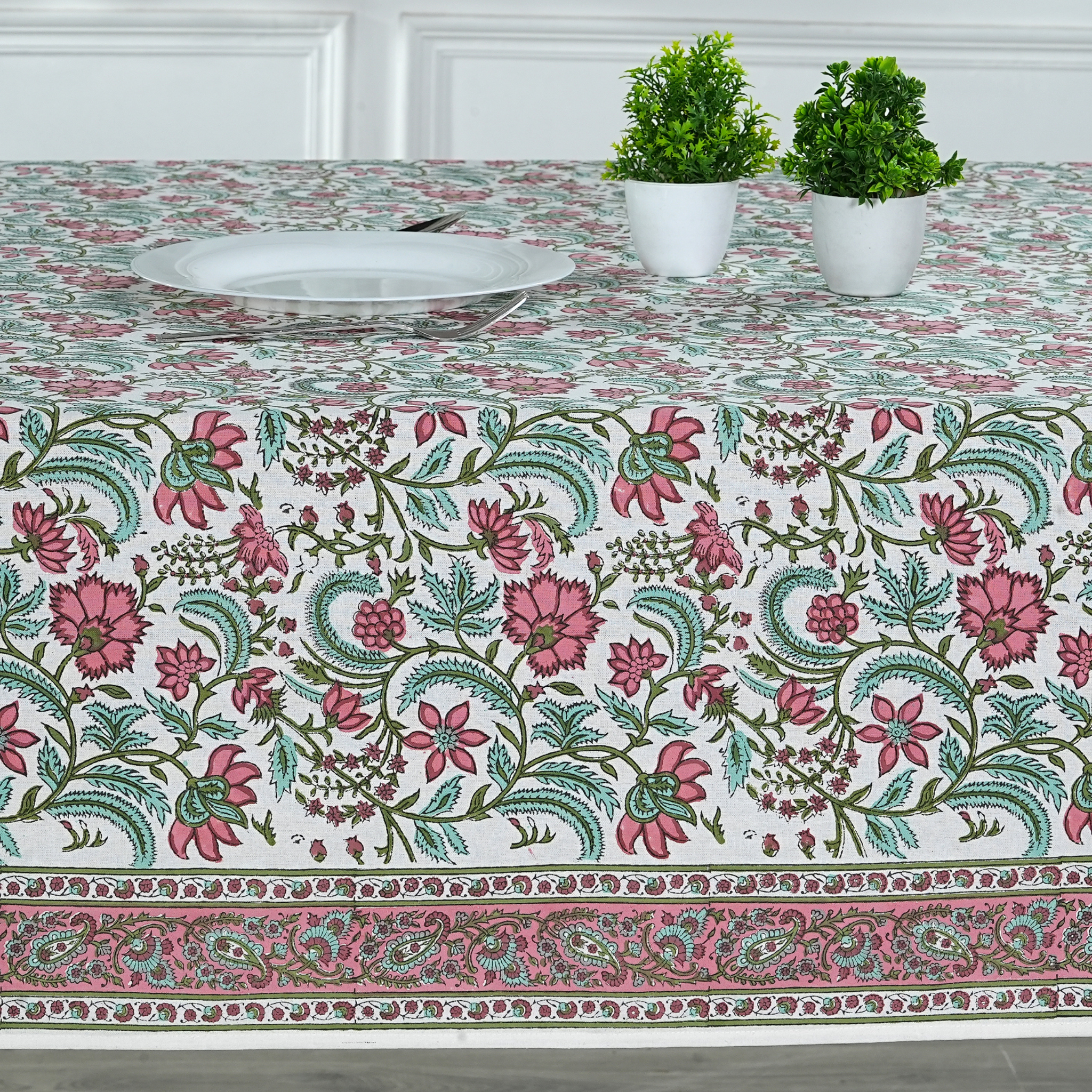 Floral patterned tablecloth on a table with two potted plants.