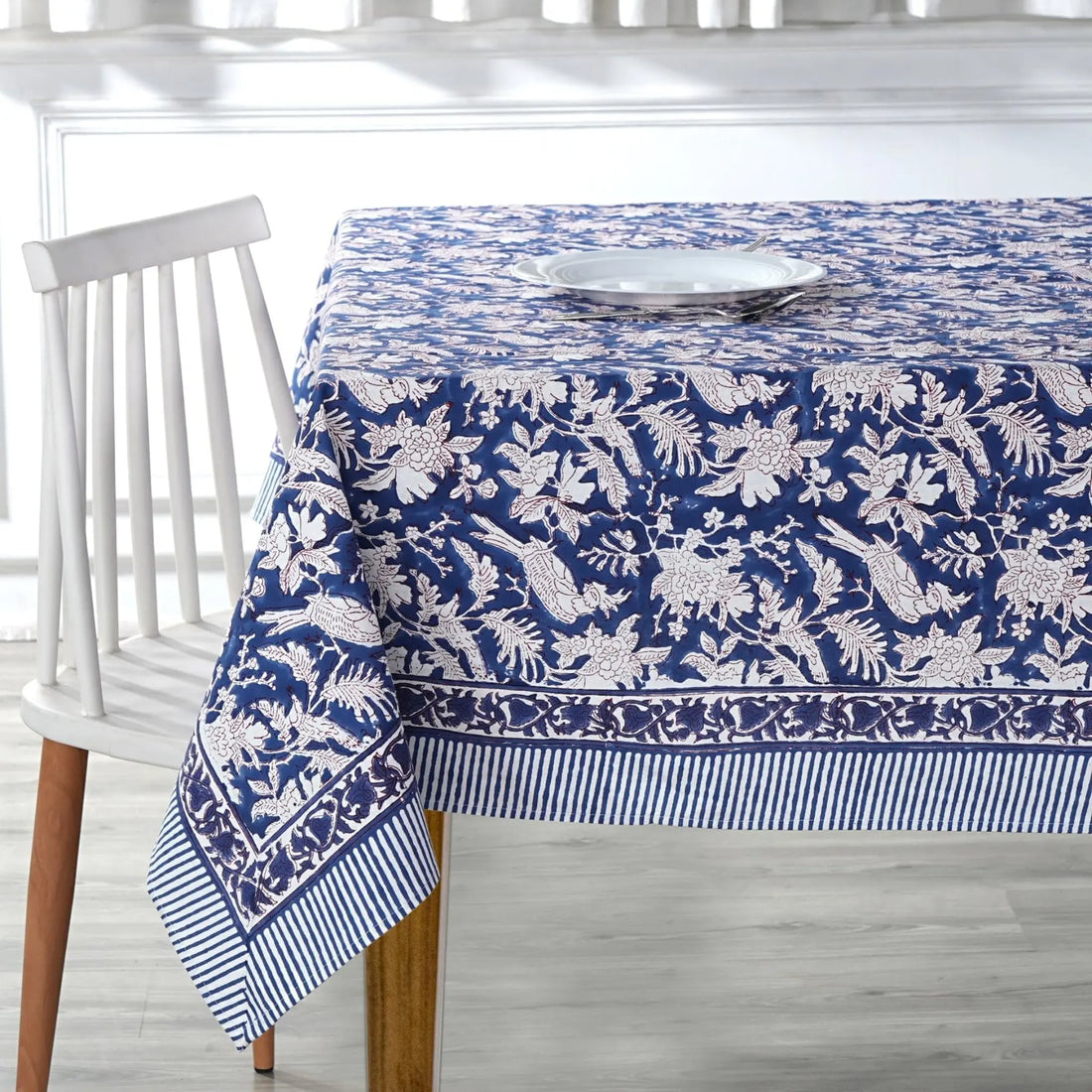 Blue and white patterned tablecloth on a wooden table with a white chair.
