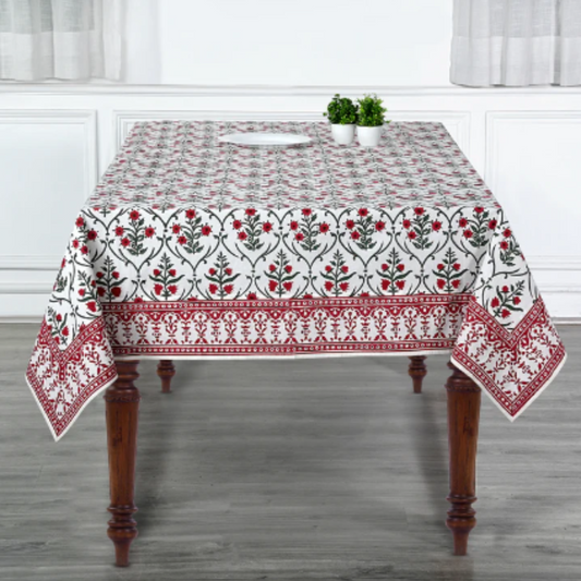 Tablecloth with floral pattern on a wooden table in a room with white curtains.