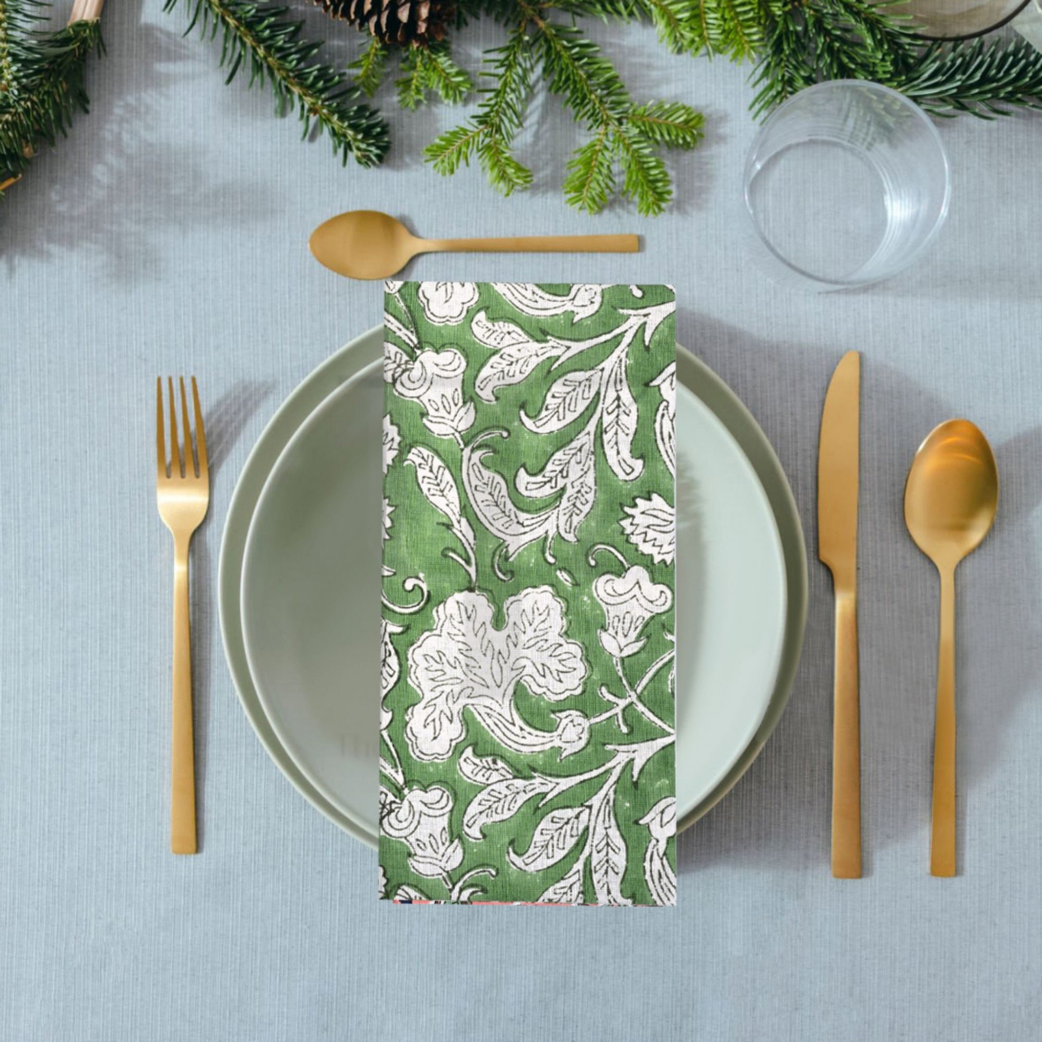 Green floral-patterned napkin on a table setting with gold cutlery and Christmas decorations.