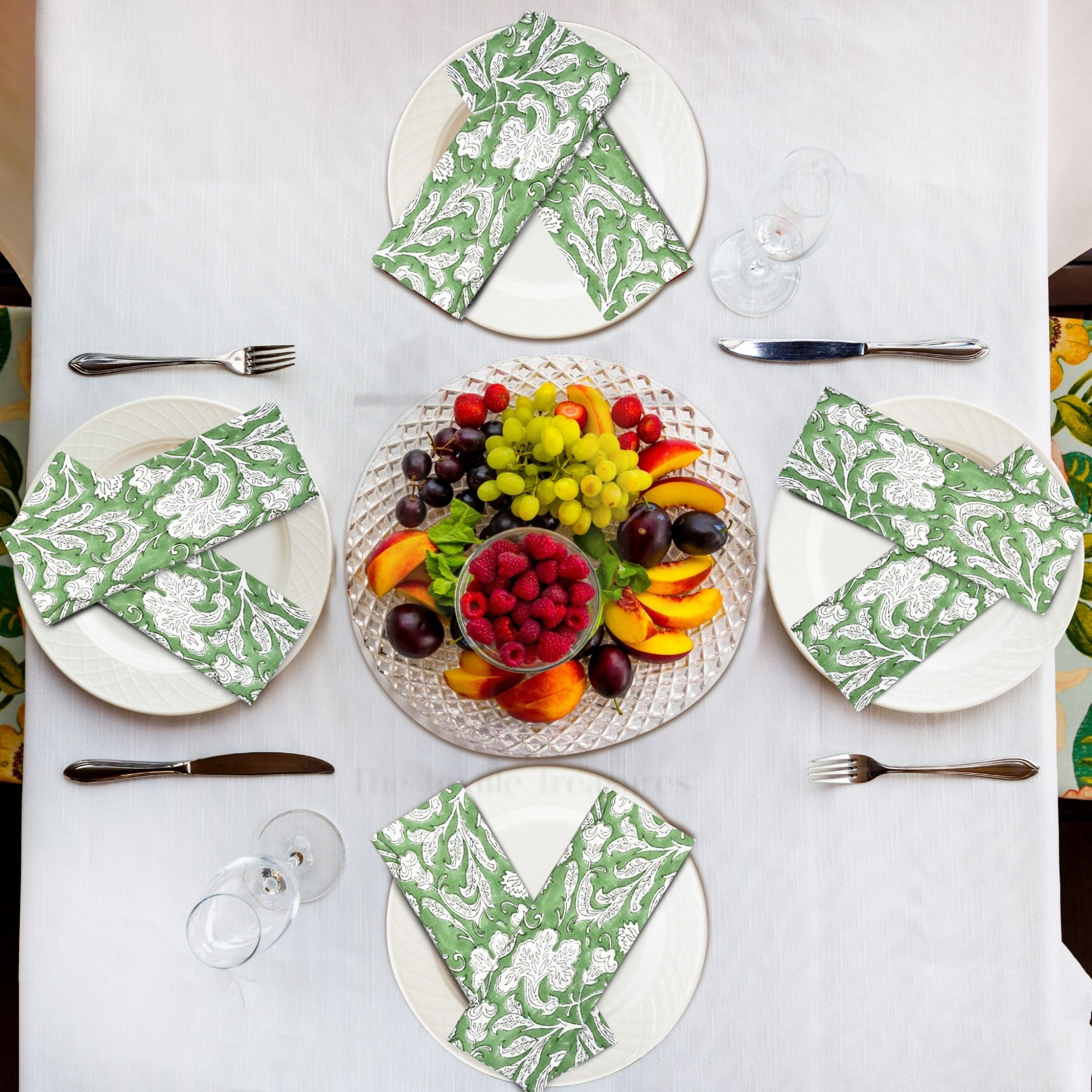 Table setting with plates, napkins, and a fruit platter on a white tablecloth.